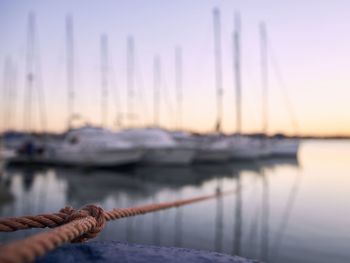 Close-up of rope against sailboats moored in sea at sunset