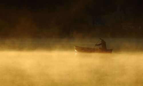 Person rowing boat in lake during sunset