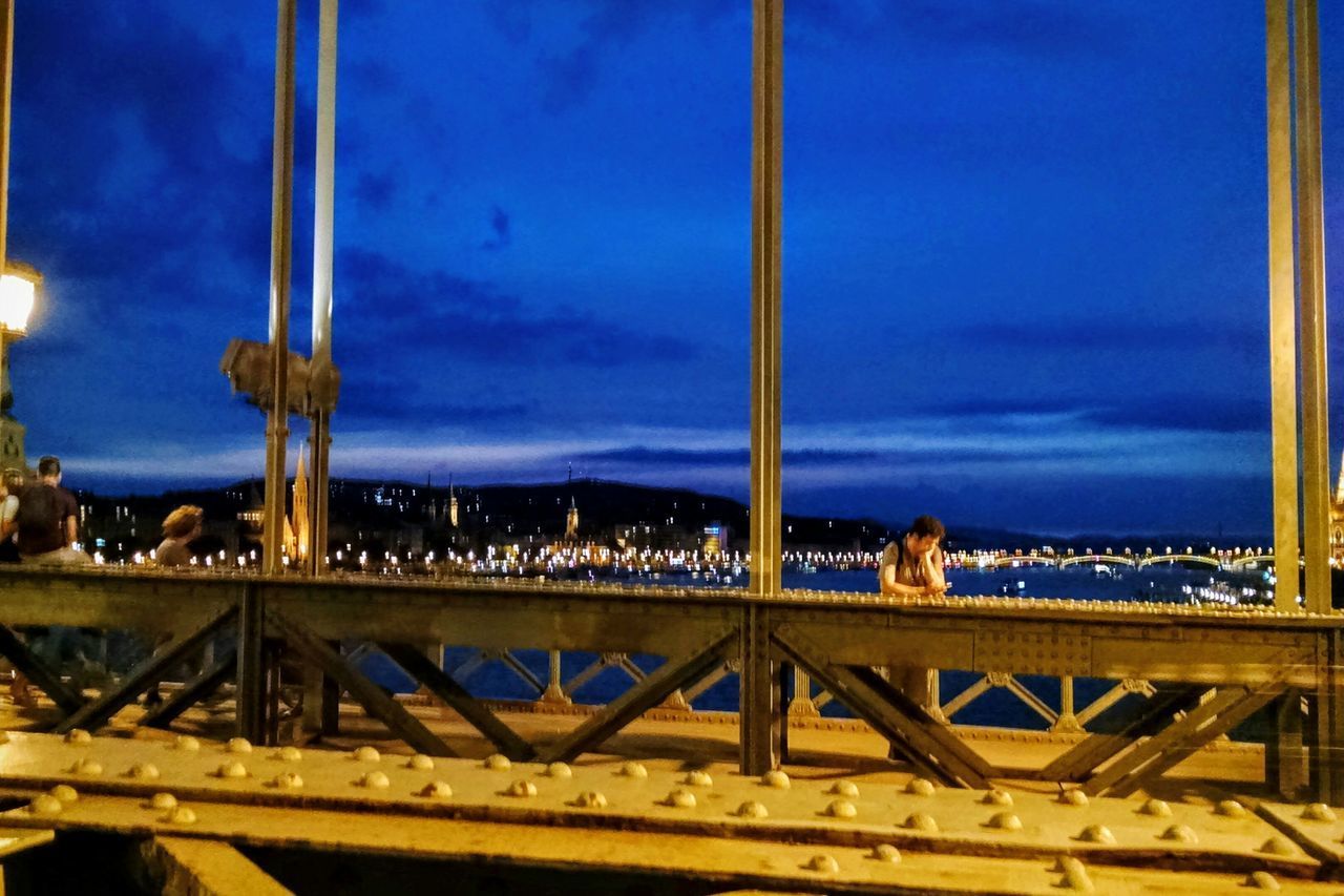 MAN STANDING BY BRIDGE AGAINST SKY