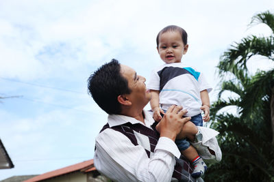 Father and baby boys against sky