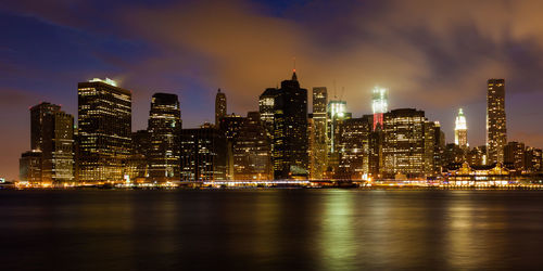 Illuminated city by river against sky at night