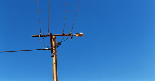 Low angle view of electricity pylon against clear blue sky