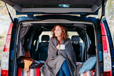 Woman holding mug while sitting in camper trailer