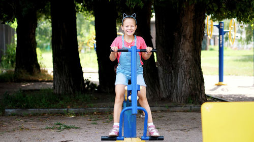 Smiling, happy eight year old girl engaged, doing exercises on outdoor exercise equipment