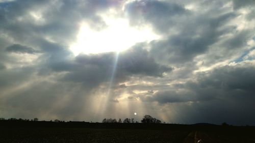 Sunlight streaming on field against sky