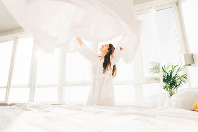 Cheerful woman holding sheet at bedroom