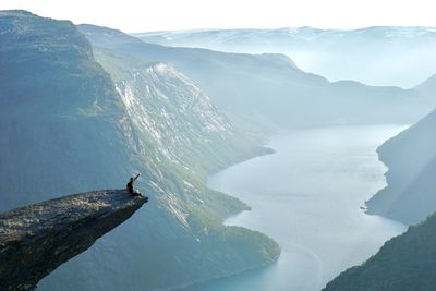 Man sitting on cliff gesturing against mountain range