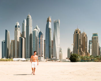 Full length of man standing on beach against skyscrapers in city