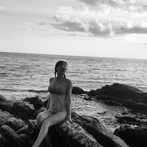 Man sitting on rock at beach against sky