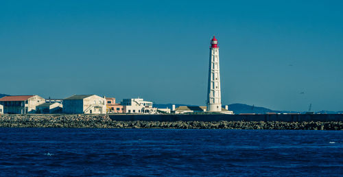 Lighthouse by building against clear blue sky