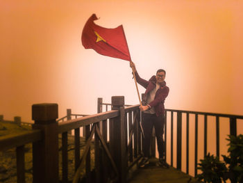 Man standing by railing against orange sky