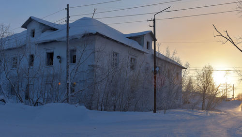 Snow covered houses against sky during sunset