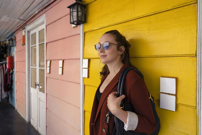 Young woman wearing sunglasses standing against yellow wall