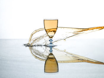 Water splashing on wineglass with reflection over white background