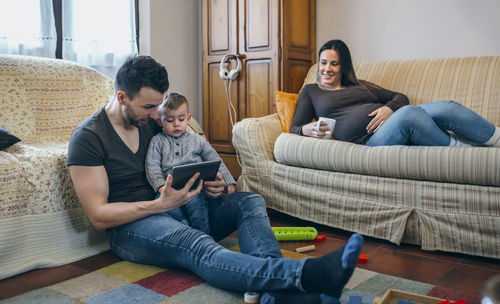 Mother looking at father with son using digital tablet while sitting in living room