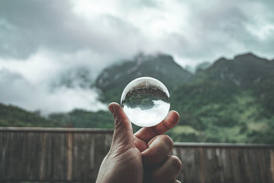 Midsection of person holding ice cream against mountains