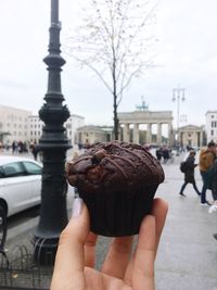 Close-up of human hand holding chocolate muffin in city