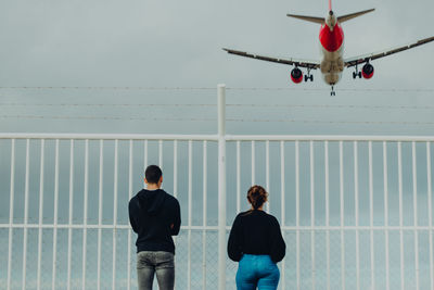 People looking at airplane flying against sky