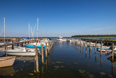 Boats moored at harbor against clear blue sky