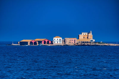 View of buildings by sea against clear blue sky