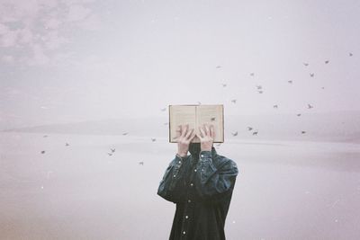 Man holding book while standing at beach