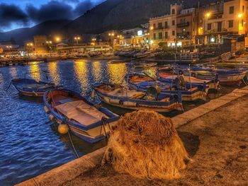 Sailboats moored in river at illuminated harbor against sky at dusk