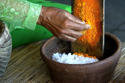Cropped image of woman grating turmeric in container