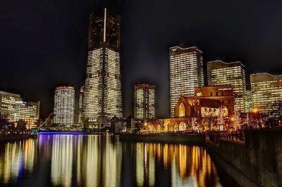 Illuminated buildings by river against sky at night