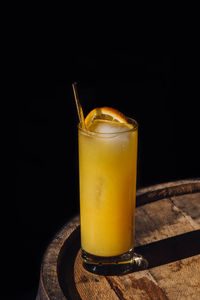 Orange juice drink in tall glass with gold straw, sitting on whiskey barrel in the sunlight