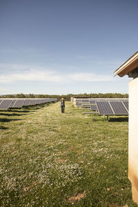 Female engineer walking on grass amidst solar panels at power station