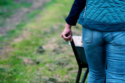 Midsection of woman pushing wheel barrow on field