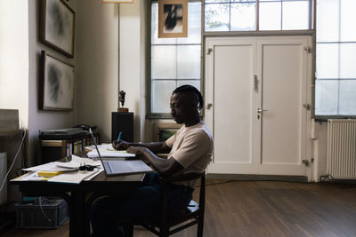 Male entrepreneur using laptop and writing on document at workplace