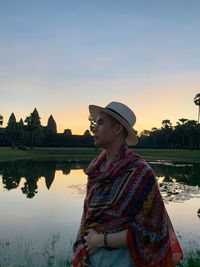 Woman standing by lake against sky during sunset