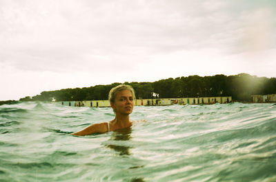 Portrait of young woman swimming in sea against sky