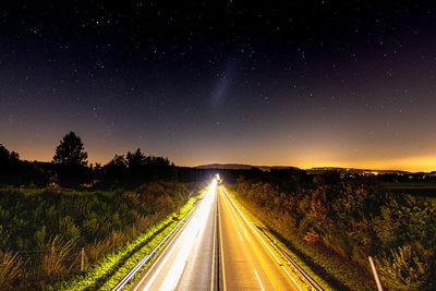 Road amidst illuminated trees against sky at night
