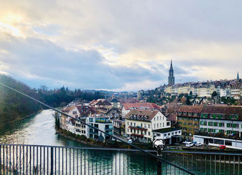 High angle view of buildings by river against cloudy sky