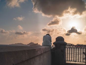 Rear view of railing by sea against sky during sunset