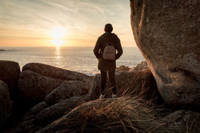 Woman, in a rocky place, watching the sunset in the coast