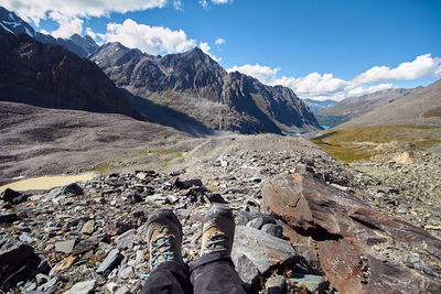 Low section of person on rock in mountains against sky