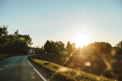 Road by trees against sky during sunset