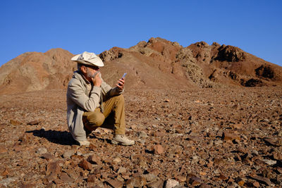 Senior man sitting on rock using mobile phone 