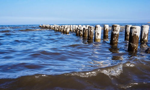 Wooden posts in sea against sky