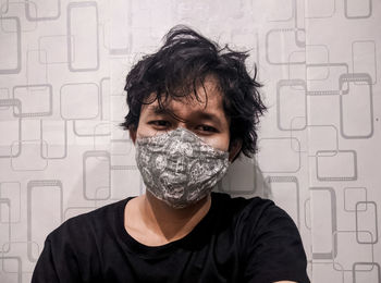 Portrait of young man wearing mask standing against wall