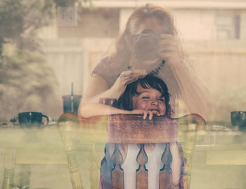 Reflection of woman photographing son seen through glass