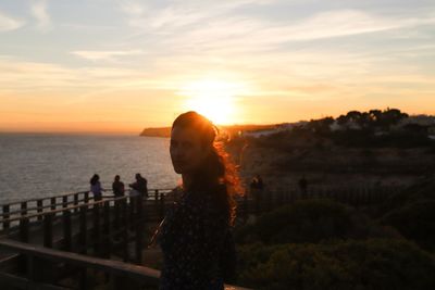 Woman standing by sea against sky during sunset