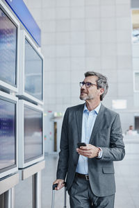 Businessman with cell phone at timetable at the airport