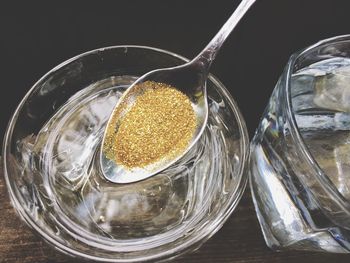 Golden glitter in spoon over glass of water