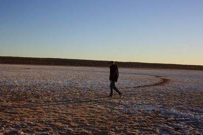 Rear view of man walking on land against clear sky