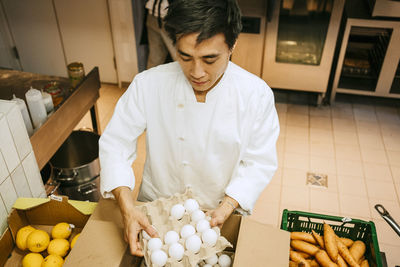 High angle view of male chef removing egg crate from box while standing in commercial kitchen