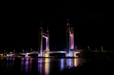 Illuminated bridge over river against sky at night